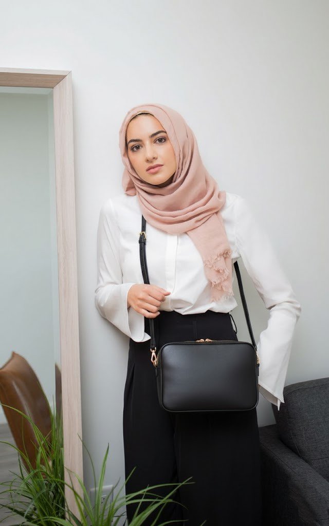 A slim, rectangular navy blue crossbody work bag made of smooth leather for office handbags for ladies, shown against a blurred city background. The bag features a long, adjustable strap and minimal silver hardware, highlighting its sleek and modern design.